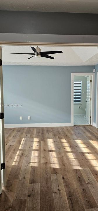 Wood-finish flooring, light blue wall paint, white trim, ceiling fan, and an open doorway
