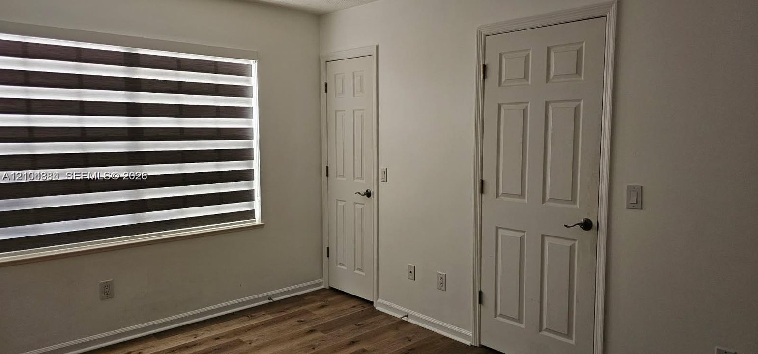 Wood-finish flooring with white baseboards, a window featuring horizontal blinds, and paneled interior doors