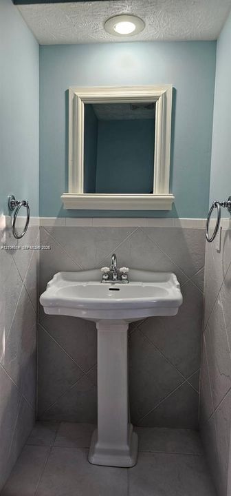 Pedestal sink with chrome faucet, framed mirror with integrated shelf, recessed ceiling lighting, and tiled walls with decorative border