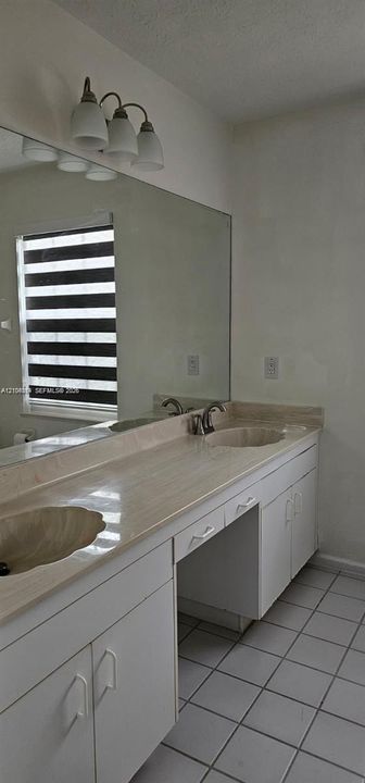 Double vanity with integrated sinks, stone-finish countertop, white cabinetry, wall-mounted mirror, and tiled flooring