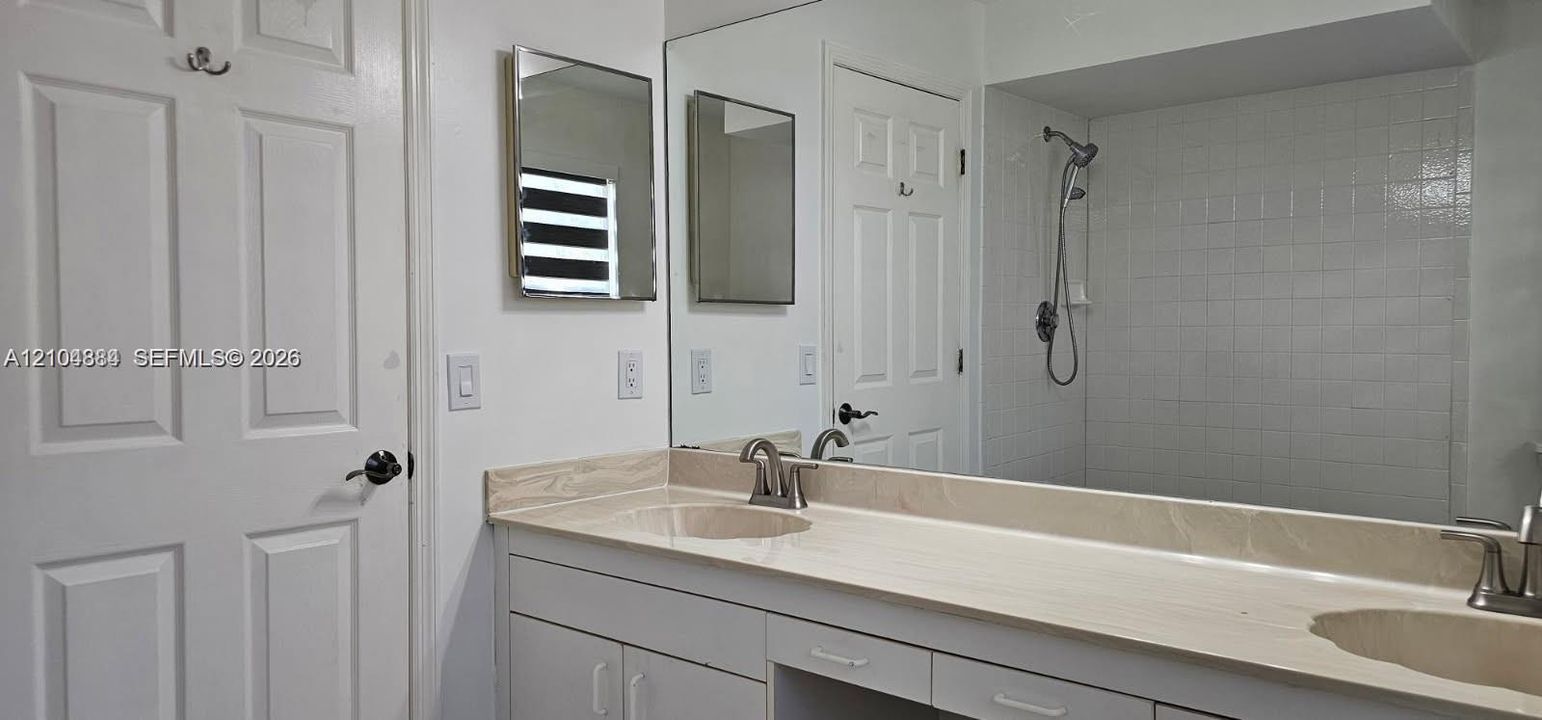 Dual vanity with integrated sinks, expansive counter space, white cabinetry, and a mirrored wall