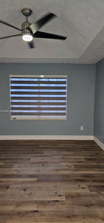 Wood-finish flooring, accent wall, modern ceiling fan with integrated lighting, and window with banded shades