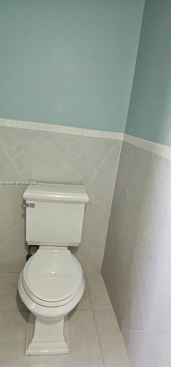 Pedestal toilet with a close-coupled design, white porcelain finish, and coordinating tiled walls featuring a decorative border