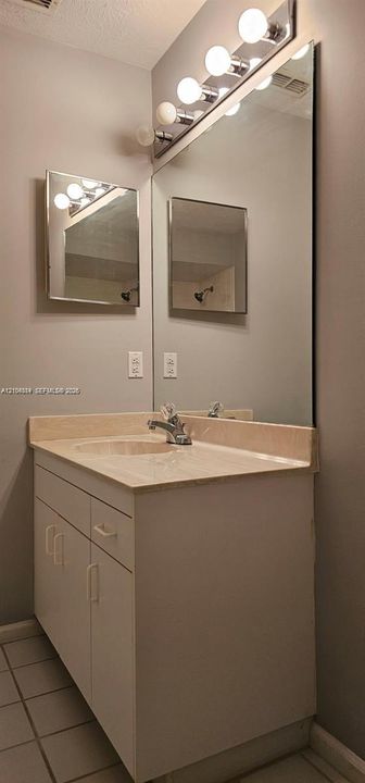 Vanity with an integrated sink, a large wall-mounted mirror, and a chrome light fixture featuring globe bulbs