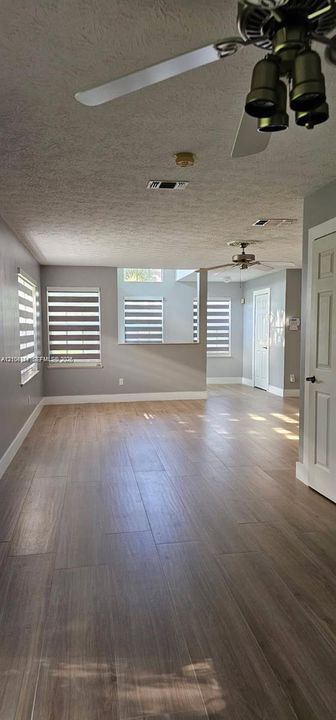 Wood-finish flooring throughout, multiple windows with blinds, ceiling fans, and a white paneled door
