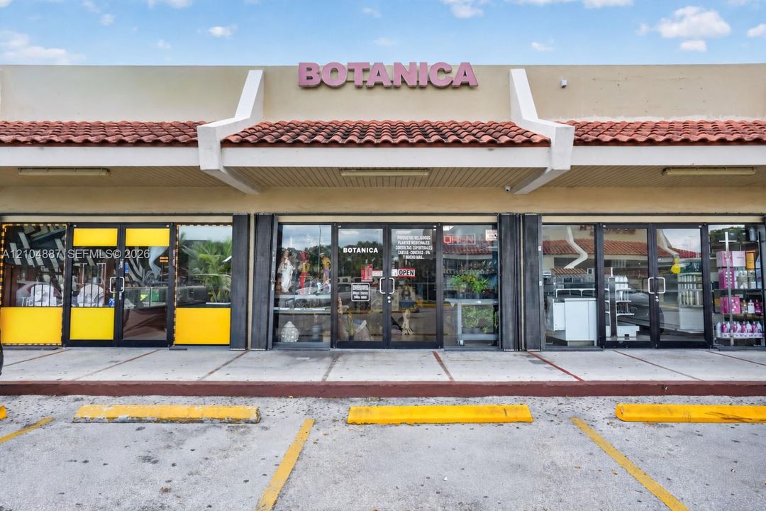 Commercial storefront featuring a clay tile roofline, concrete sidewalk, glass-paned entrance doors, and overhead exterior lighting