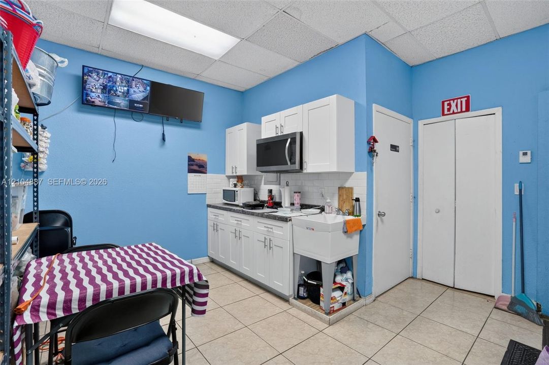 Kitchen area featuring white shaker-style cabinetry, a white utility sink, built-in microwave, tile flooring, and a suspended drop ceiling