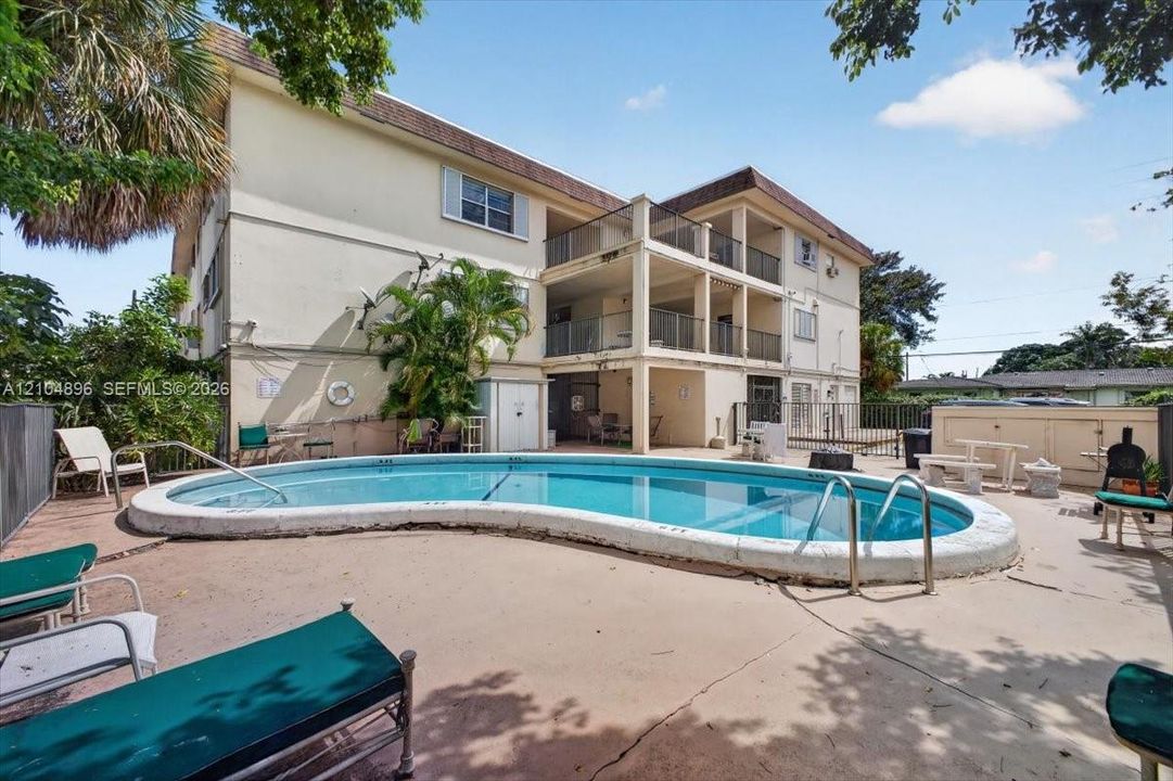In-ground kidney-shaped swimming pool with a concrete deck, multi-level exterior balconies with metal railings, and stucco siding