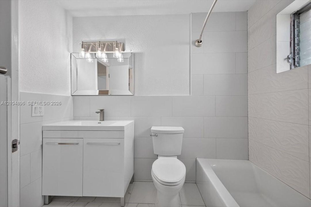 Bathroom featuring a white vanity cabinet, rectangular countertop sink with a chrome faucet, large rectangular wall tile, and a built-in bathtub with a curved shower rod