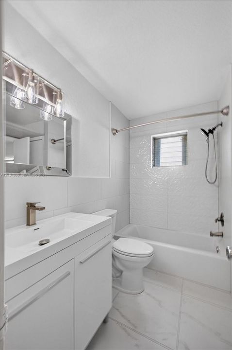 Bathroom featuring a white vanity with a rectangular sink, metallic faucet, wall-mounted mirror with integrated light fixture, and a white tile bathtub surround