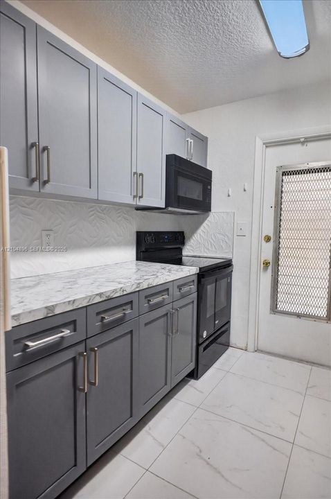 Kitchen featuring dual-tone cabinetry with modern hardware, stone-patterned countertops, textured backsplash, and large-format tile flooring