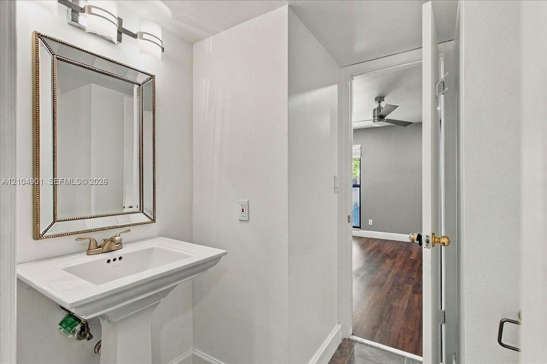 Pedestal sink with metallic faucet, wall-mounted beveled-edge mirror, and multi-light vanity fixture