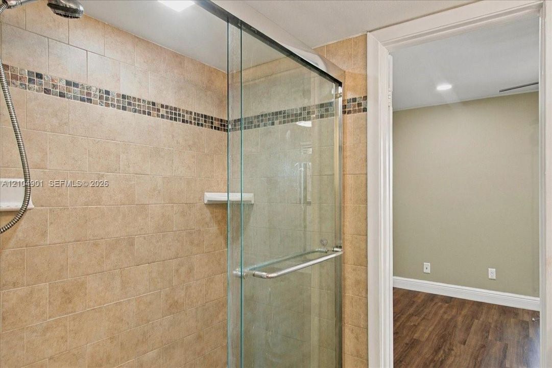 Walk-in shower featuring glass enclosure, wall-mounted shower head, mosaic tile accent border, and ceramic tile surround