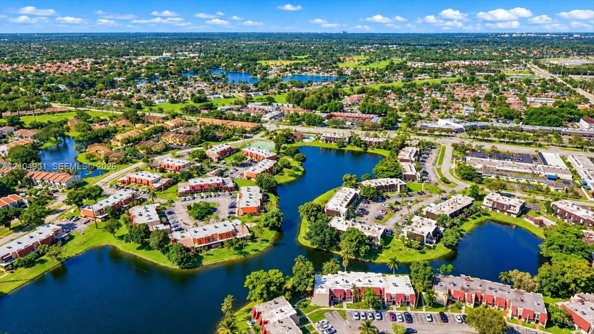 Aerial perspective of residential community featuring multiple interconnected bodies of water, mature landscaping, paved surface parking, and multi-story structures with flat rooflines