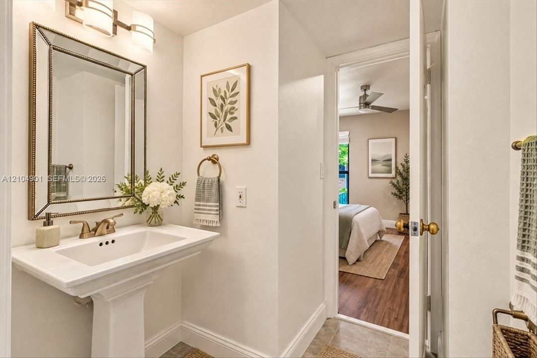 Pedestal sink with a brass-finish faucet, framed wall mirror, and dual-bulb wall-mounted lighting fixture