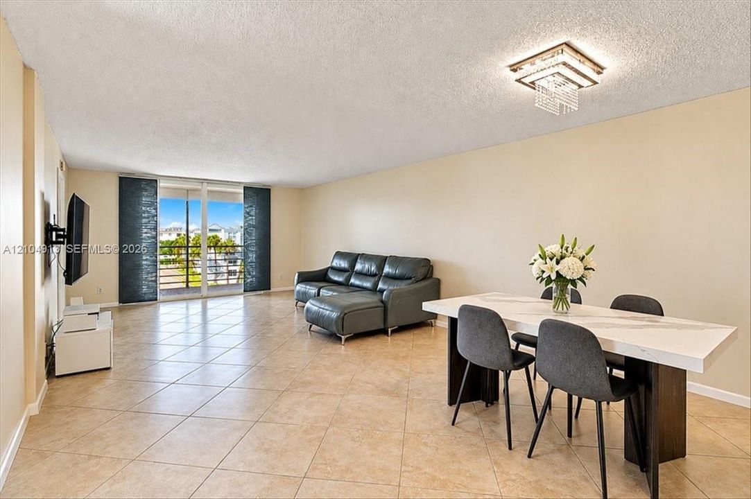 Open-concept living space featuring ceramic tile flooring, a tiered crystal flush-mount light fixture, and floor-to-ceiling sliding glass doors opening to an exterior balcony
