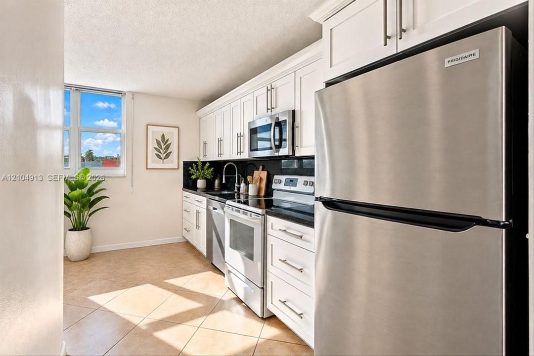 Kitchen featuring white shaker-style cabinetry, dark stone countertops, stainless steel appliances, and tile flooring