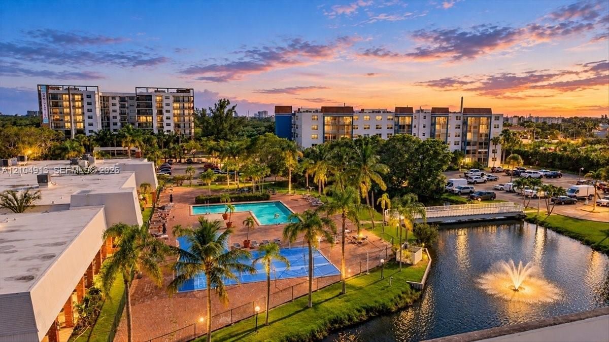 Outdoor swimming pool featuring a paved deck, surrounding palm trees, an aerating water fountain, and an adjacent pond