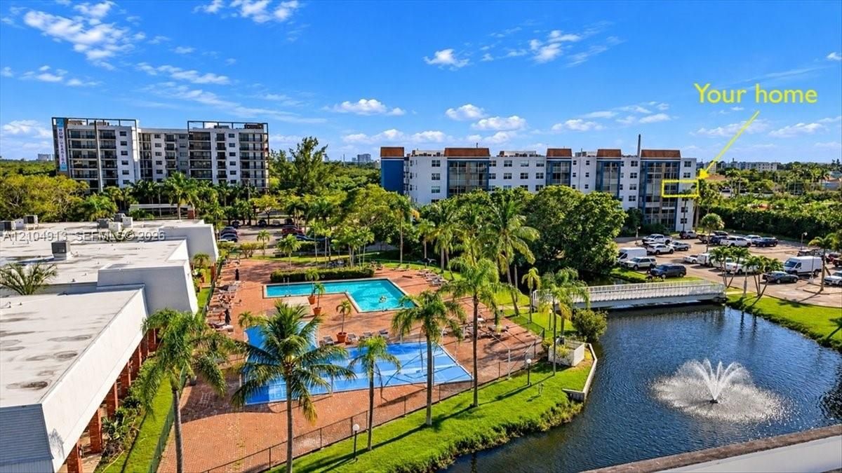 Aerial perspective of a multi-story residential building complex featuring an outdoor swimming pool, paved pool deck, water feature with fountain, and mature palm trees