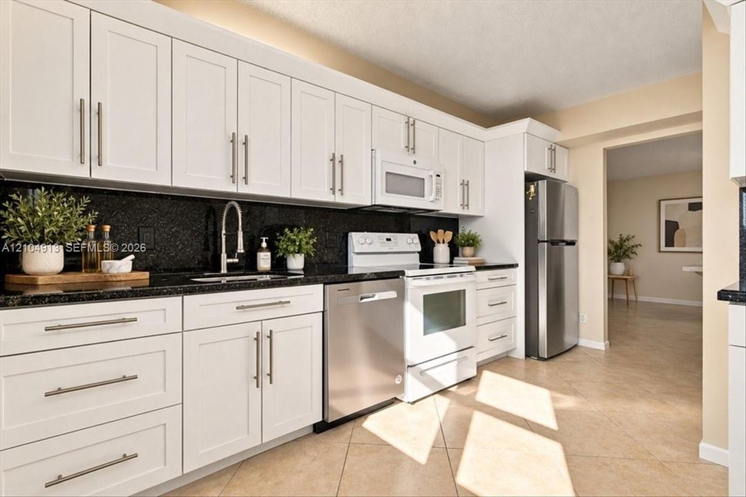 Kitchen featuring white shaker-style cabinetry, dark stone countertops, stainless steel appliances, and tile flooring