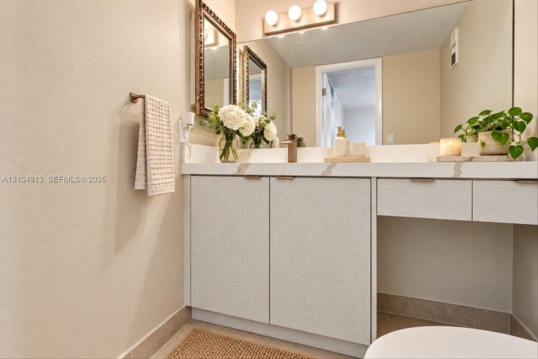 Custom vanity with stone-patterned countertop, integrated under-mount sink, metallic hardware, and full-width wall mirror with three-bulb overhead lighting