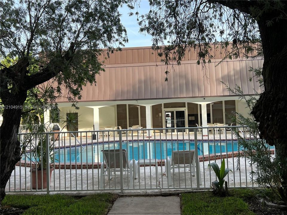 Swimming pool with brick coping, surrounded by a paved deck and enclosed by a metal perimeter fence, featuring a covered patio with structural columns