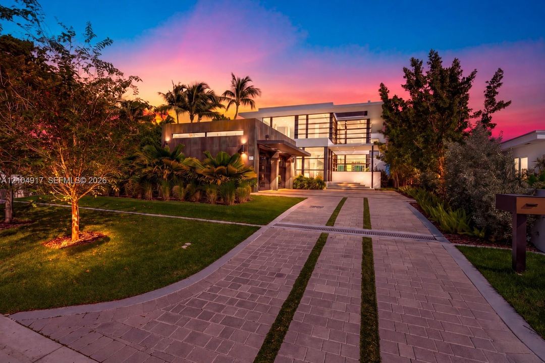 Contemporary multi-level residence featuring a stone-clad facade, extensive glass curtain walls, paver driveway with integrated grass ribbons, and professionally landscaped grounds