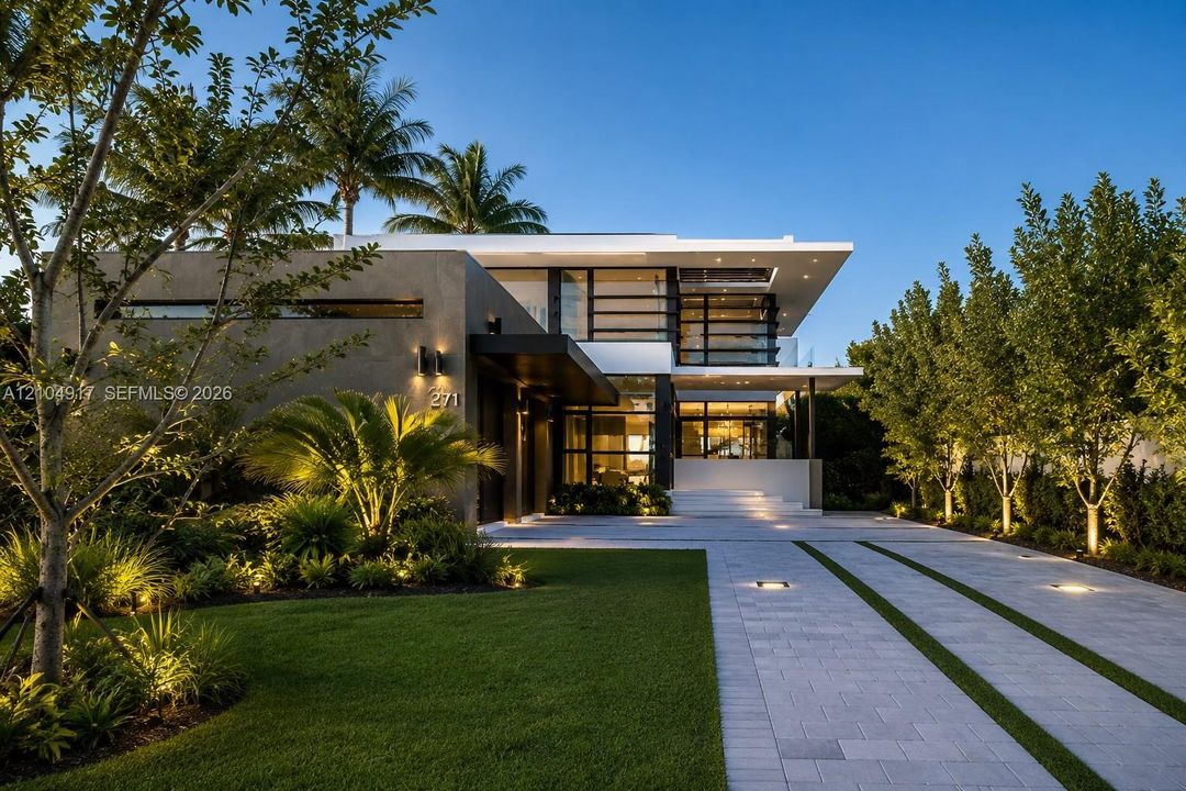 Modern two-story architectural exterior featuring smooth stucco finish, expansive glass windows, integrated landscape lighting, and a paved driveway with linear grass accents