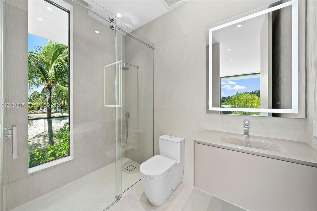 Modern bathroom featuring a glass-enclosed shower with a rainfall showerhead, a floating vanity with an integrated sink, and an illuminated mirror