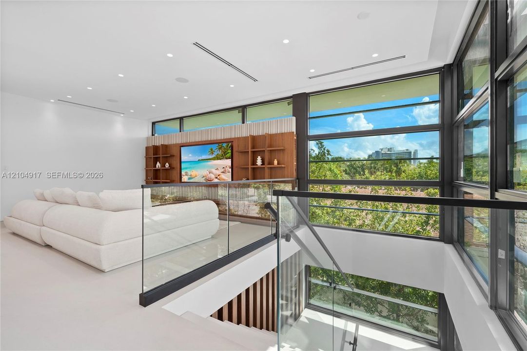 Upper-level lounge with expansive windows, a built-in media center with integrated shelving, recessed lighting, and a glass-paneled railing