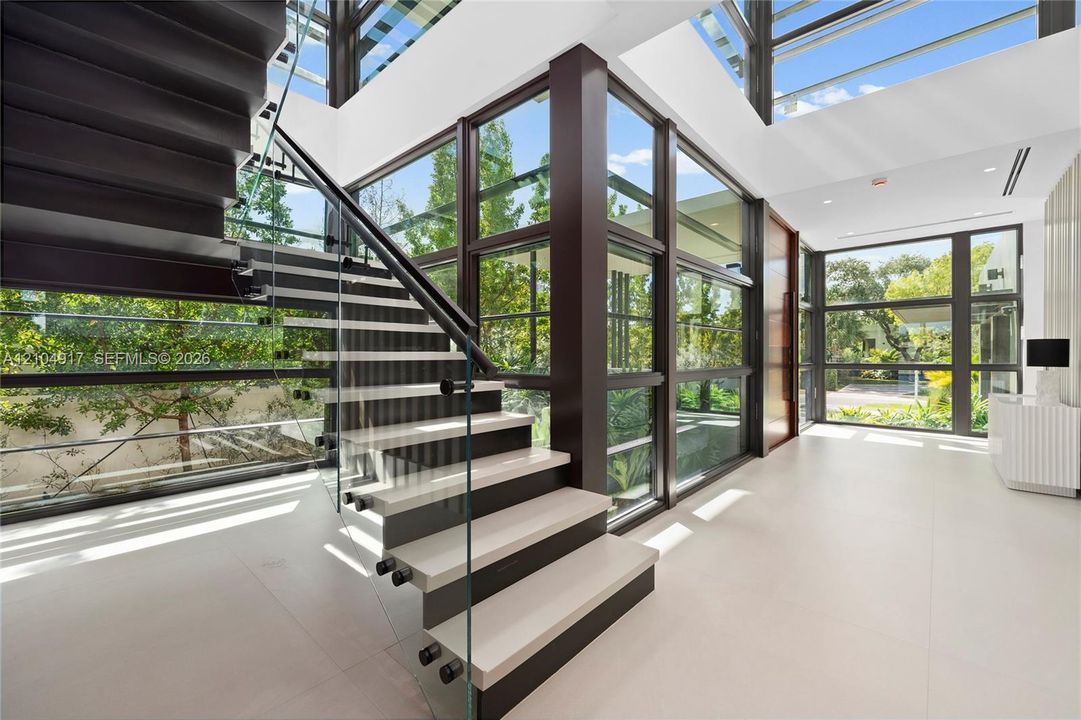 Modern staircase with glass railing, dark wood risers, light-toned treads, and large format floor tiling