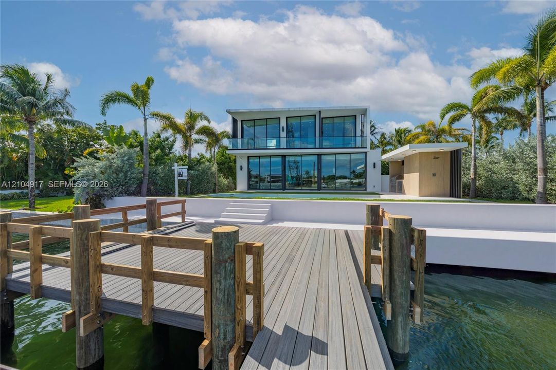 Modern waterfront residence featuring expansive floor-to-ceiling glass paneling, a multi-level deck, a private dock with wood-finish decking, and a swimming pool
