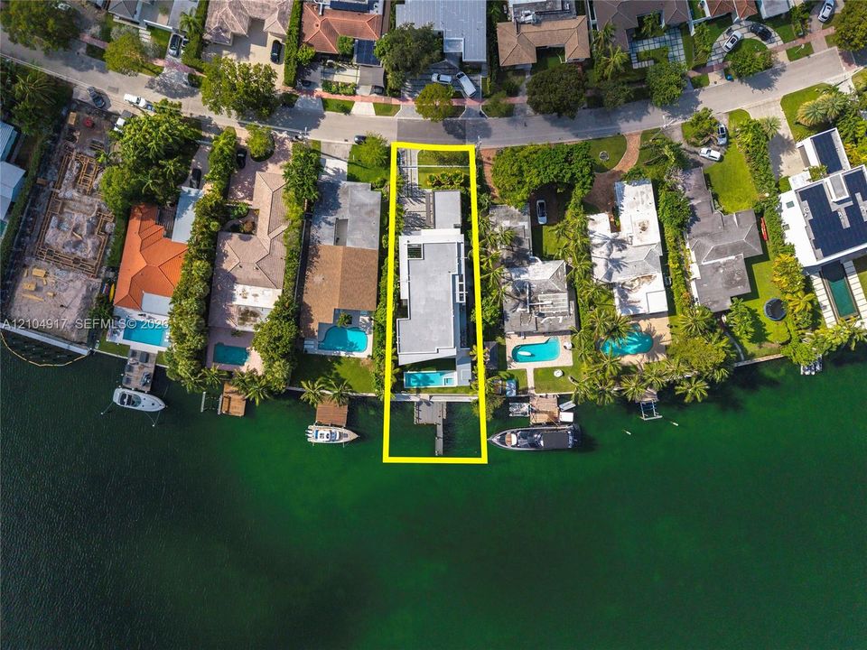 Waterfront property featuring a private dock, rectangular swimming pool, concrete driveway, and established perimeter landscaping