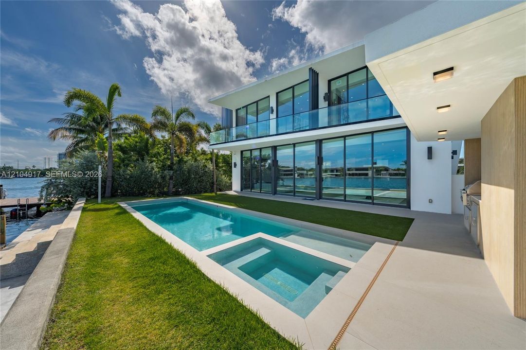 Contemporary waterfront exterior featuring floor-to-ceiling glass walls, a multi-level balcony with a glass railing, an inground swimming pool with a built-in spa, and a concrete patio