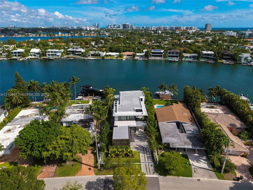 Waterfront residence featuring deep-water dockage, multi-level flat roof architecture, expansive floor-to-ceiling glass fenestration, paved motor court, and mature tropical landscaping
