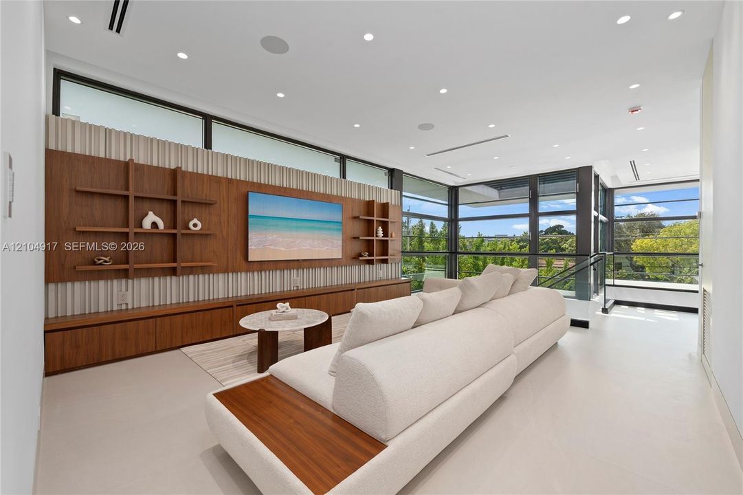 Built-in wood-finish media console with integrated shelving, floor-to-ceiling windows, recessed lighting, and light-toned flooring