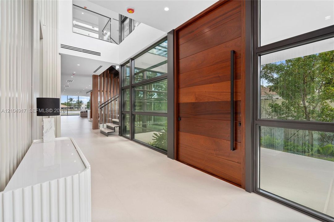 Grand entry featuring a large wood-panel door, floor-to-ceiling glass panels, and a two-story foyer
