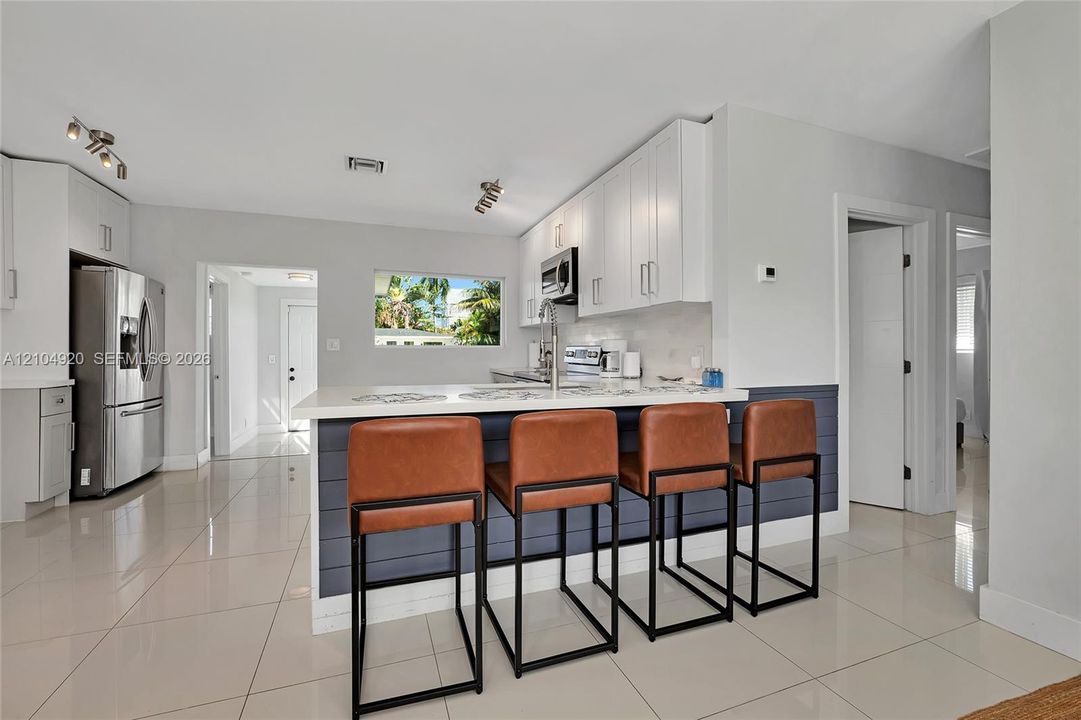 Kitchen featuring white cabinetry, quartz countertops, a shiplap-accented breakfast bar, polished tile flooring, and stainless steel appliances