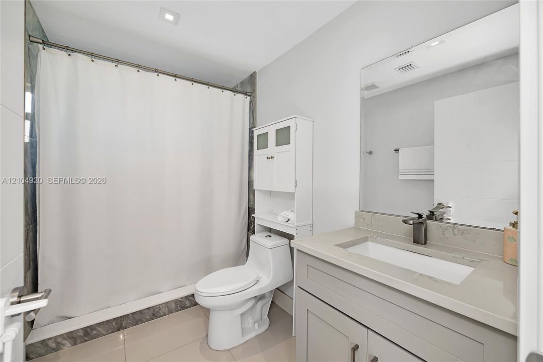 Bathroom featuring a stone-surface vanity with an integrated rectangular sink, wall-spanning mirror, one-piece toilet, and tile shower surround