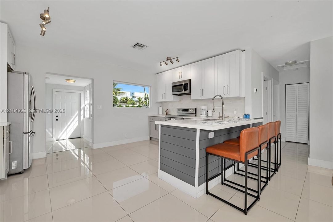 Kitchen featuring white cabinetry, an island with grey shiplap paneling, stainless steel appliances, and large-format tile flooring