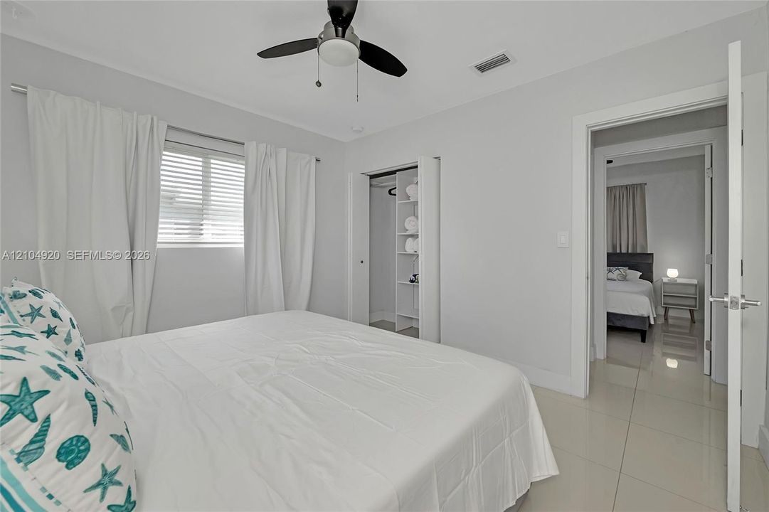 Neutral-toned interior featuring oversized tile flooring, a ceiling fan with integrated lighting, a built-in closet shelving system, and horizontal window blinds