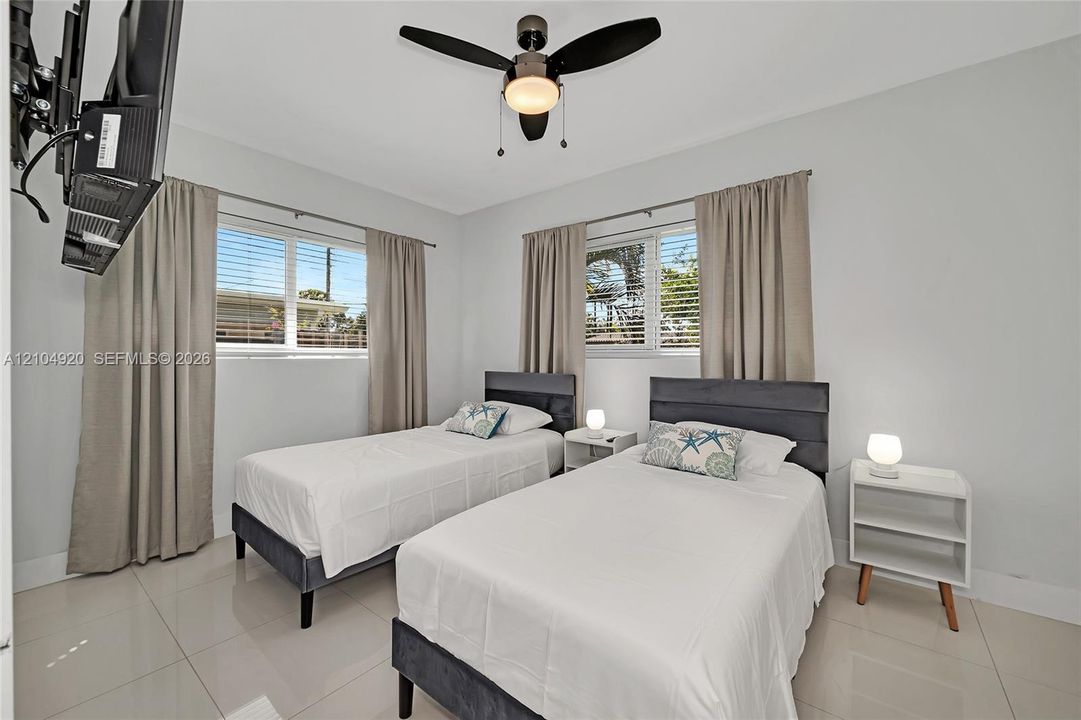 Neutral-toned interior space featuring light-colored tile flooring, multiple windows with horizontal blinds, and a contemporary ceiling fan with integrated lighting