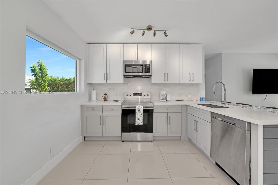 Kitchen featuring shaker-style cabinetry, stainless steel appliances, light-toned stone-finish countertops, tile flooring, and multi-directional track lighting