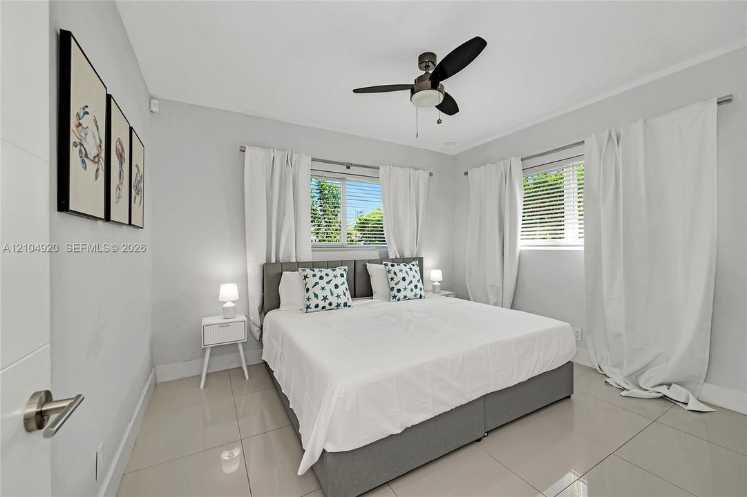 Neutral-toned interior featuring large-format tile flooring, multi-pane windows with horizontal blinds, and a central ceiling fan with integrated light fixture