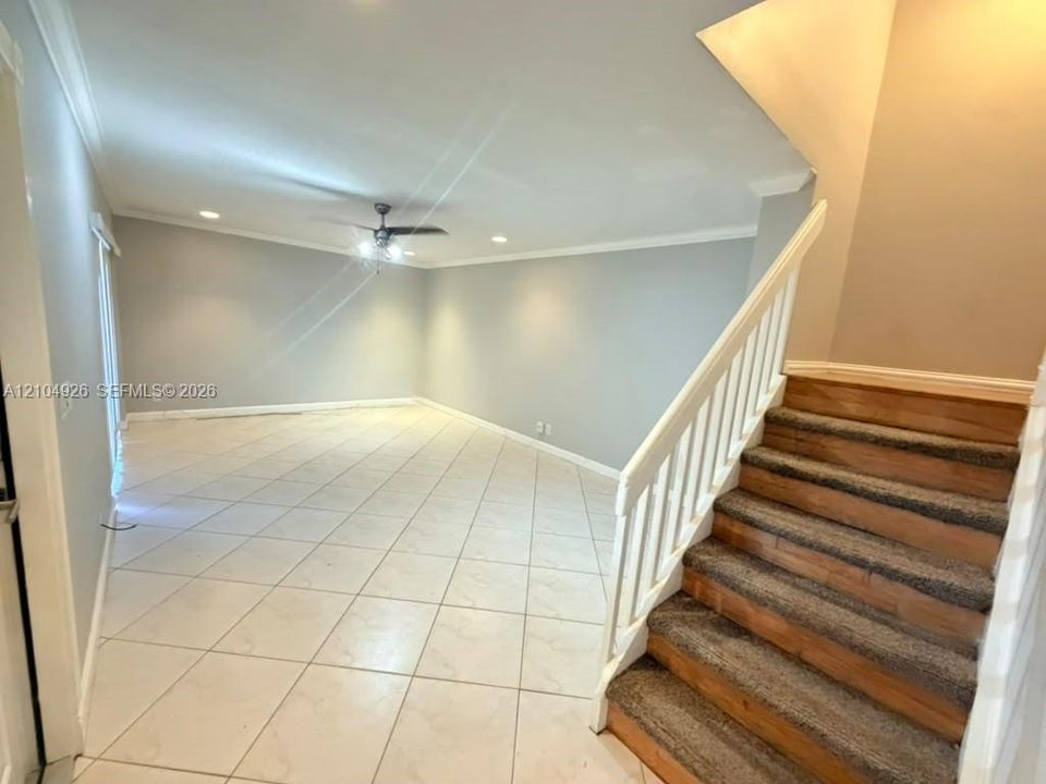 Open-concept interior featuring light-colored floor tiling, recessed lighting, a ceiling fan, and a staircase with a white balustrade and wood-finish treads