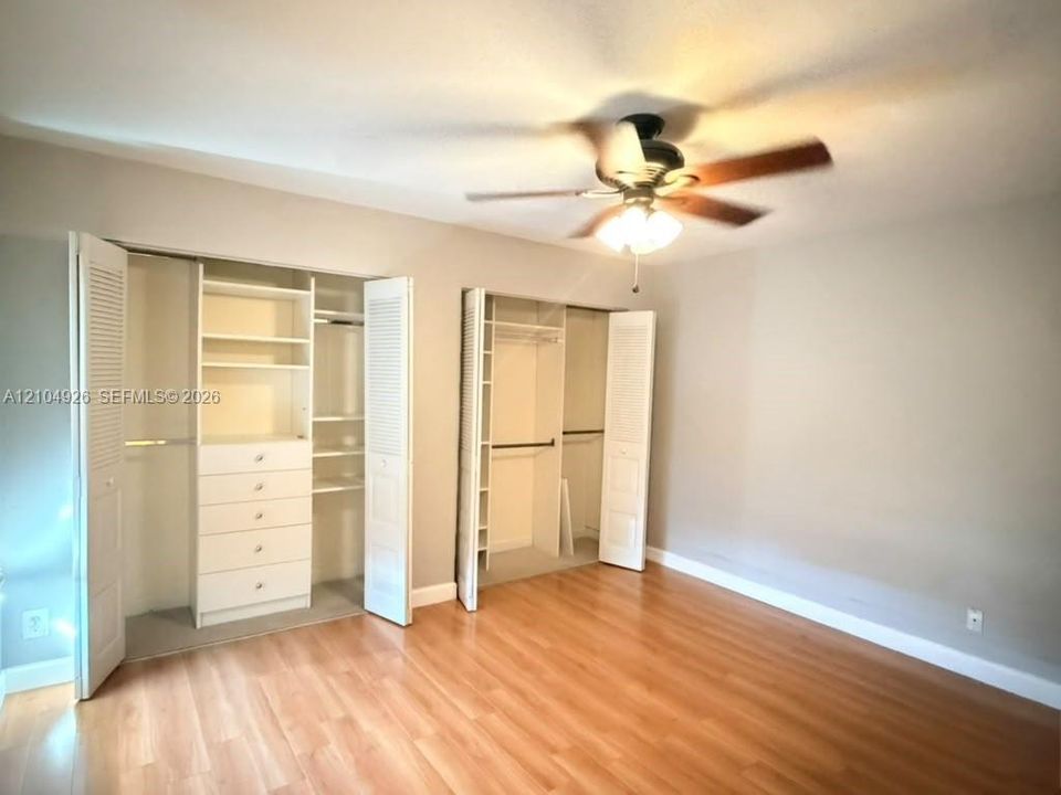 Wood-finish flooring, dual closets with louvered doors, built-in drawer storage, adjustable shelving, and a ceiling fan with integrated lighting