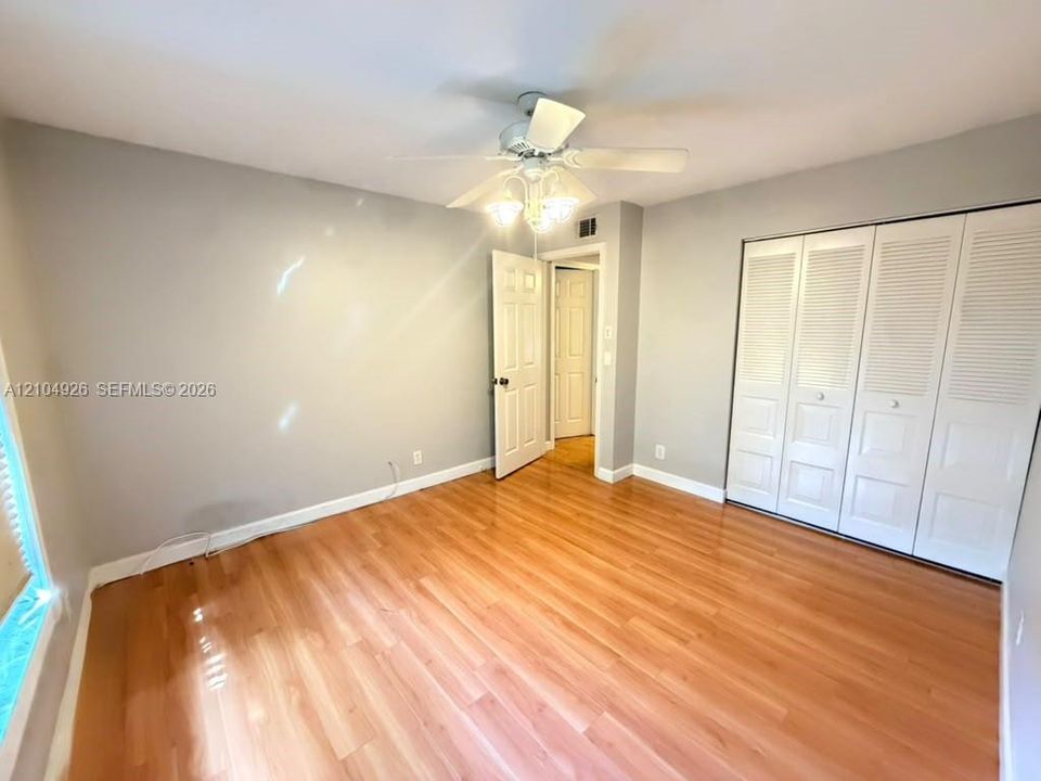 Room featuring wood-finish flooring, white four-panel bifold closet doors, and a ceiling-mounted light fixture with a fan