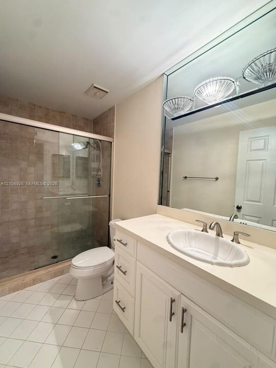 Bathroom featuring a vanity with an integrated basin, a large wall-mounted mirror, a glass-enclosed shower with tiled surround, and ceramic tile flooring