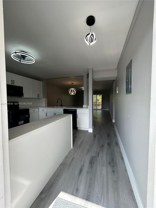Kitchen featuring white cabinetry, solid-surface countertops, black appliances, wood-finish flooring, and contemporary geometric pendant lighting