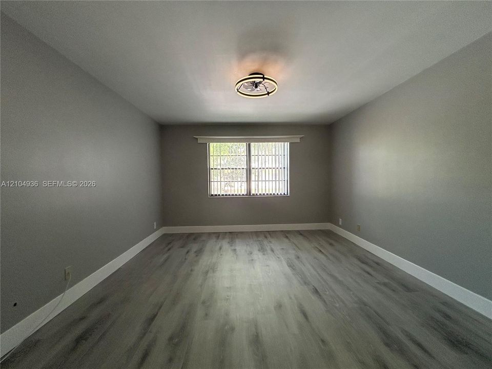 Neutral-toned interior room featuring wood-finish flooring, a multi-pane window with vertical blinds, and a circular flush-mount ceiling fixture